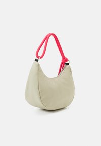 Beige halvmåneformad handväska med synlig dragkedja och bright pink knuten rep-handtag på en vit bakgrund.