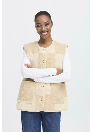 Beige fleece vest with button closure and patch pockets, featuring a textured pattern and sleeveless design, layered over a white long-sleeve top.