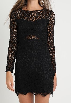 Czarna koronkowa sukienka z długimi rękawami, ozdobiona kwiatowym wzorem i wycięciem. Dół sukienki wykończony jest koronką z frędzlami.