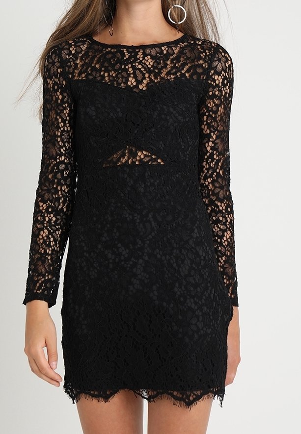 Robe en dentelle noire à manches longues, présentant un motif floral et un détail découpé. L'ourlet est orné de dentelle à franges.