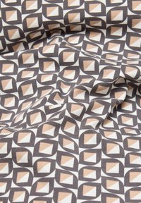 Weiches Gewebe mit einem sich wiederholenden geometrischen Muster aus braunen und beigen Rauten auf einem weißen Hintergrund, sanft gefaltet dargestellt.