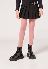 Svart plisserad kjol, rosa glittriga strumpbyxor och blanka svarta ankelstövlar med chunky sula och dragkedjedetalj.