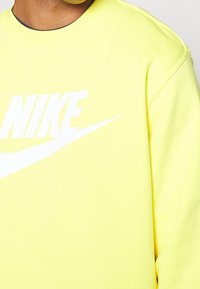 Mikina Nike v jasně žluté barvě, s velkým bílým logem přes hrudník. Design s kulatým výstřihem a texturovaným materiálem.
