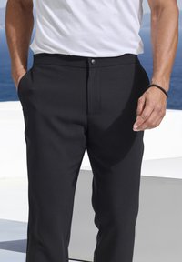 Schwarze, maßgeschneiderte Hosen mit glatter Textur, flacher Vorderseite und einem Knopfverschluss. Taschen an beiden Seiten; lässige Passform.