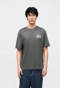 Siva pamučna majica kratkih rukava, okruglog izreza i malim bijelim natpisom "SRETNI PRAZNICI" na lijevoj strani prsa.