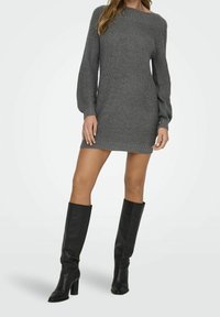 Abito maglione grigio a maniche lunghe, con una trama a coste e un colletto sceso, abbinato a stivali neri con tacco al ginocchio.