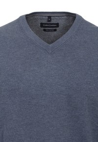 Temno modra v-neck jopica iz pima bombaža, ki ima teksturiran pleten vzorec in majhno logo na levi strani. Oznaka velikosti srednje je vidna.