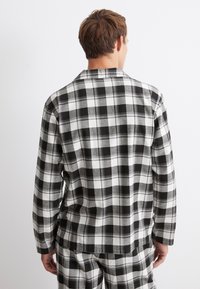 Musta-valkoinen ruudullinen flanellipaita rentoa istuvuutta, pitkät hihat ja kaulus, jossa on näkyvä rakenne ja ruutukuvio.