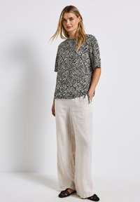 Top corto a maniche corte con motivo zebra in bianco e nero abbinato a pantaloni larghi in lino beige chiaro e scarpe slip-on nere in tessuto intrecciato.