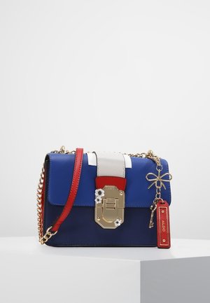 Blauwe en marineblauwe handtas met rood-witte band, gouden sluiting met bloemdetails en gouden ketting met strik- en sleutelbedels op een witte ondergrond.