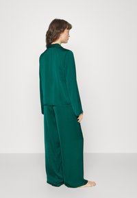 Ensemble en deux pièces de couleur vert profond, composé d'un top à manches longues de coupe décontractée et d'un pantalon large, fabriqués dans un tissu lisse avec un minimum de détails.