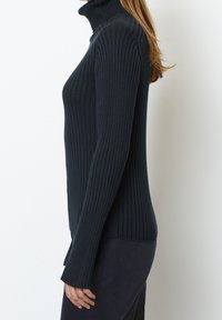 Ribbineuletulla turtleneck-neuleella tummansininen väri, jossa pitkät, istuvat hihat ja kapeneva siluetti. Pehmeä pinta ja sivuhalkiot helmassa.