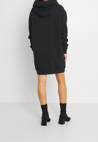 Robe sweat à capuche noire avec une poche kangourou et une grande capuche, dotée de manches longues et d'une coupe décontractée, associée à des chaussettes noires montantes jusqu'aux genoux et des talons blocs.