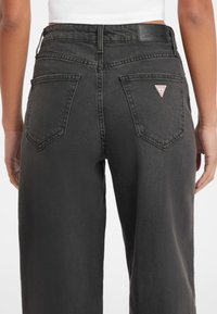 Jeans negros de cintura alta con un corte relajado, que cuentan con bolsillos traseros, detalles cosidos y un pequeño logo de la marca en el bolsillo derecho.