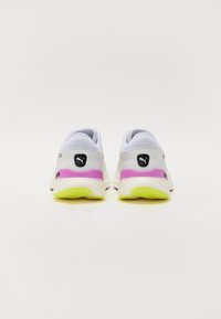 Zapatillas deportivas blancas con un acento rosa, que presentan una parte superior texturizada, un logo negro en el talón y una suela de color amarillo neón.