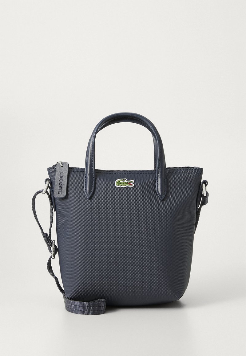 Borsa a mano blu navy con tessuto strutturato, due manici superiori e una tracolla rimovibile. Presenta un piccolo logo Lacoste e una chiusura con zip.