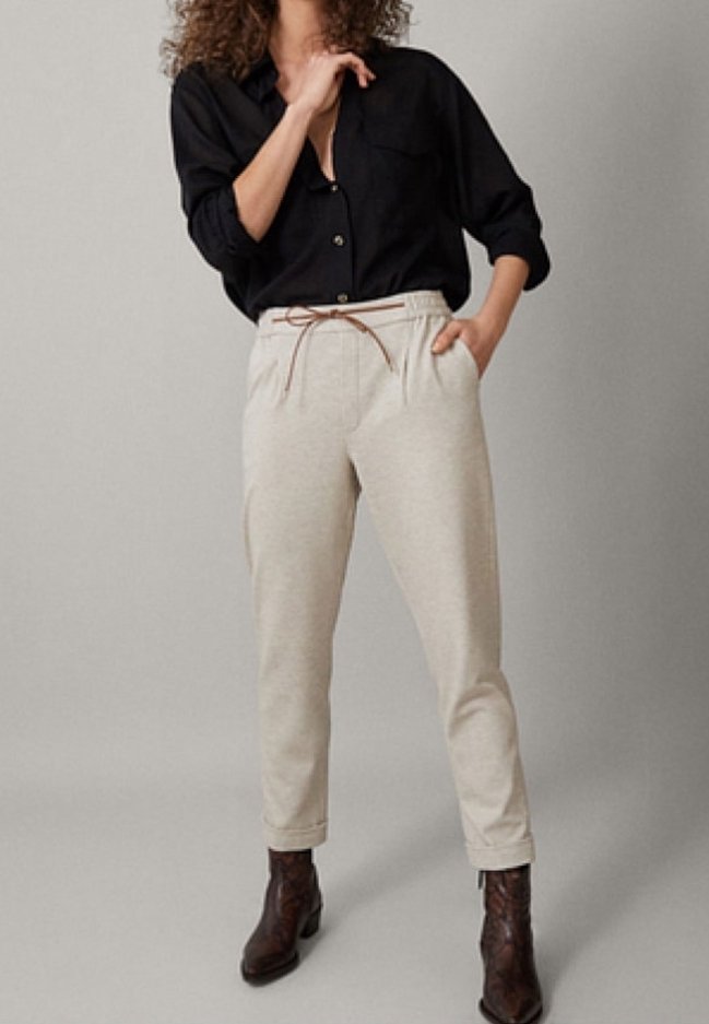 Beige Jogginghose mit elastischem Bund, braunem Kordelzug, Seitentaschen und schmal zulaufendem Bein; kombiniert mit einem schwarzen Hemd und braunen Stiefeln.