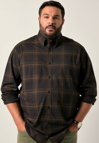 Donker geruite shirt in bruin en zwart, met een button-down kraag, lange mouwen en zwarte knopen. Casual gedragen over groene broek.