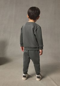 Grauer Sweatshirt und passende Jogginghose, weicher Stoff, entspannte Passform, gerippte Bündchen und Saum, kombiniert mit hellen Sneakern. Einfaches und stimmiges Design.