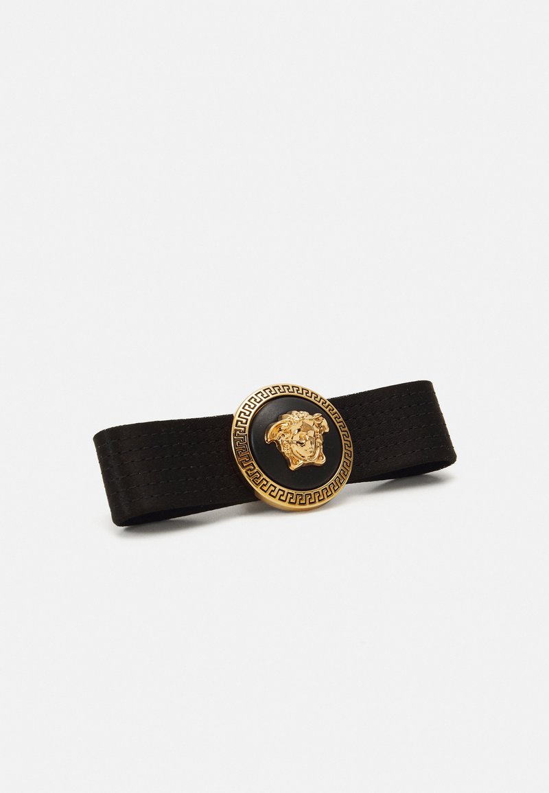 Black elastic strap featuring a circular gold-tone buckle with a lion motif and intricate Greek key pattern around the edge.