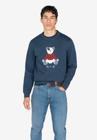 Sudadera marina con un oso polar bordado en un suéter rojo. Material suave, puños acanalados y diseño de cuello redondo. Corte casual que combina con jeans azules.