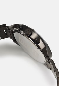 Schwarze Edelstahl-Uhr mit einem strukturierten Armband, ausgestattet mit drei Tasten an der Seite und einem glatten, runden Gehäuseboden mit einem Logo.