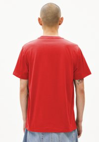T-shirt en coton rouge avec un col rond et des manches courtes. Le dos présente un design simple sans motifs ni accents supplémentaires.
