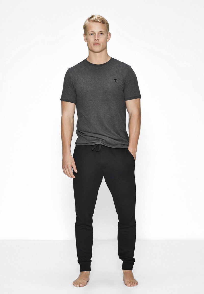 Kortærmet grå T-shirt med rund halsudskæring, parret med sorte tapered joggingbukser med elastisk talje og manchetter ved anklerne.