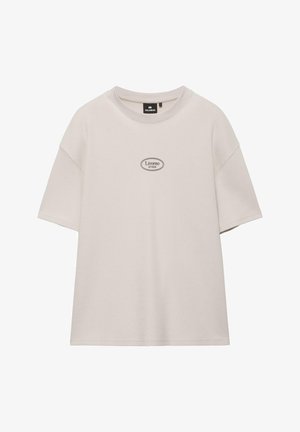 Beżowa koszulka z krótkim rękawem i okrągłym dekoltem, z nadrukiem na środku klatki piersiowej z napisem „Livorno 57020” w owalnej ramce.