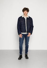 Jeansjacka med en lätt fuskpälskrage, mörkblå tvätt, två bröstfickor och knäppning, tillsammans med tajta blå jeans och svarta stövlar.