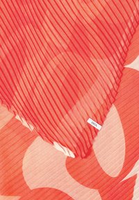 Tissu plissé rouge superposé à un tissu à motif floral dans des tons de rouge et de rose, avec une petite étiquette "CECIL" visible.