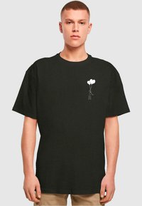 Svart bomulls T-skjorte med et hvitt grafisk motiv av en figur som holder to ballonger. Designet er enkelt med korte ermer og rund hals.