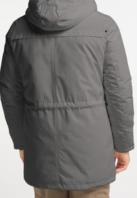 Veste à capuche grise avec une finition lisse et brillante. Dispose d'une taille élastique, de poches latérales et de détails de coutures le long des manches et du dos.