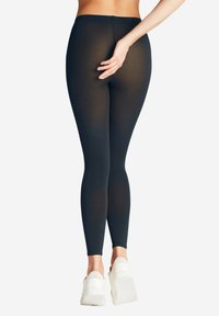 Leggings neri realizzati in un tessuto trasparente e elastico. Design a vita alta con una texture liscia. Accentati da una sottile cucitura posteriore.