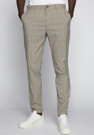 Beige karierte Hose mit Fronttaschen, schmaler Passform und Knopfverschluss, kombiniert mit weißen Sneakern. Glatte Stoffoberfläche.