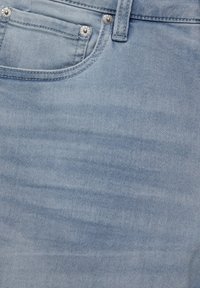 Gros plan sur un jean en denim bleu clair montrant la poche avant, les rivets en métal et les détails de couture des passants de ceinture.