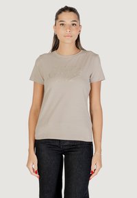 T-shirt in cotone beige con maniche corte, che presenta un logo lucido "GUESS Los Angeles" in un font corsivo sul petto.