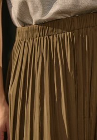 Jupe plissée marron avec une surface texturée, dotée d'une taille élastique et de plis verticaux, capturée sous un angle révélant les détails du tissu.