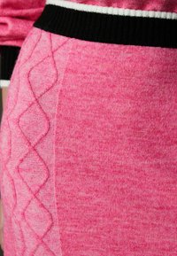 Fuksia roosa, kootud legginsid, millel on tekstureeritud teemantmustrit külgedel ja must ribikreen valgete triipudega.
