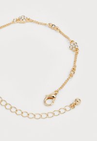Gold chain bracelet with decorative flower motifs and clear rhinestones. Features a lobster claw clasp and adjustable length with a ball detail.