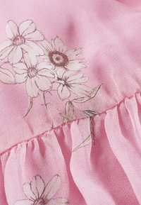 Stoff mit floralem Muster in sanftem Rosa, der zarte weiße Blumen mit braunen Konturen zeigt und einen gerafften, rüschigen Rand für Textur hat.
