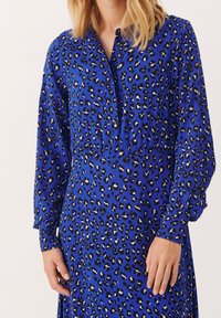 Blå leopardmönstrad klänning i lättviktigt material, med en knappställd halsringning, långa ärmar och en draperad midjedesign.