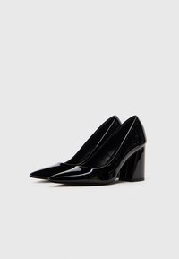 Sorte laklæder højhælede pumps med spids tå og kraftig hæl, der har en glat, blank tekstur og et strømlinet design.