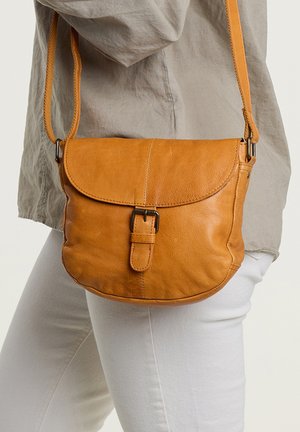 Brun læder crossbody taske med en buet form, magnetisk flaplukning og justerbar rem. Har synlige sting og en subtil tekstur.