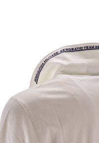 Polo bianco con colletto ripiegato che presenta una scritta in blu che dice "AERONAUTICA MILITARE - TEAM AEROBATICO." Tessuto e design dalla superficie liscia.