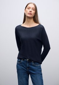 Marineblaues Langarmoberteil mit einem U-Boot-Ausschnitt, aus weichem Stoff; kombiniert mit blauen Jeans aus Denim mit Knopfverschluss und Taschen.