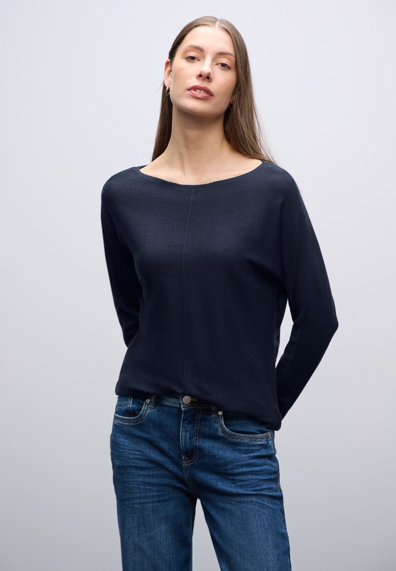 Marineblaues Langarmoberteil mit einem U-Boot-Ausschnitt, aus weichem Stoff; kombiniert mit blauen Jeans aus Denim mit Knopfverschluss und Taschen.