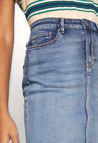 Jeanskjol i en medelblå tvätt med hög midja, med framfickor, en dragkedja och sömdetaljer längs sömmarna.