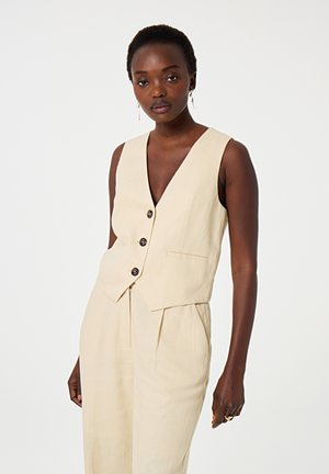 Beige Leinenweste mit tiefem V-Ausschnitt, fünf Knöpfen, Seitentaschen und taillierter Passform, kombiniert mit passenden, lockeren Hosen.