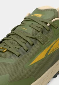 Green athletic shoe with textured mesh upper, featuring yellow branding and accents, and flat laces. Lightweight sole with a patterned design.